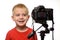 Smiling blond boy in front of the camera lens. Little video blogger. White background