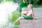 A smiling blond boy sits on a pier near the shore of a lake with a circle and makes splashes from the water, a child learns to