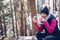 Smiling blond hiker is sitting on a tree stump drinking hot tea and eating a hamburger on a mountain trail.