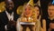 Smiling blond woman in birthday hat blowing candles on cake, friends applauding