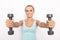 Smiling blond woman in blue tip holds two dumbbells in hands. Selective focus. White isolated background