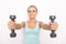 Smiling blond woman in blue tip holds two dumbbells in hands. Selective focus. White isolated background