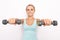 Smiling blond woman in blue tip holds two dumbbells in hands. Selective focus. White isolated background