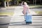 Smiling blond woman with suitcase crossing the road and waving