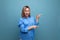 smiling blond young woman in casual shirt shows hands to the right on a baner on a blue background with copy space