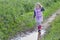 Smiling blonde girl with loose fair hair walking on dirt road rain puddle on purple clover flowers meadow