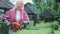 Smiling blonde girl in plaid shirt holding trimmer for shaping bushes in garden.