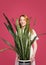 Smiling blonde holding flower sansevieria on pink background