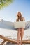 Smiling blonde sitting on hammock using laptop