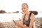 Smiling blonde sports woman with earphones sitting on beach