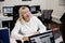 Smiling blonde woman middle-aged office worker in a white jumper sits at a computer in the office and negotiates