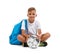 A smiling boy with a ball and a blue satchel sitting in a yoga pose. Happy child isolated on a white background. Sports