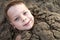 Smiling boy buried in sand on beach