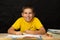 Smiling boy decides homework, sitting at a desk. Cheerful schoolboy writes homework with his left hand