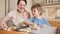 Smiling boy with mother making biscuits and putting them on baking sheet. Children cooking with parents, little chef