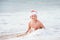 Smiling boy in Santa`s hat swims on ocean surfline. Christamas a