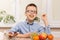 Smiling boy sits at the table and eats fruit. He has grape fruit in his teeth.