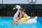 Smiling boys float on a swan inflatable ring in a swimming pool.