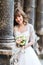 Smiling bride holding wedding bouquet on background of old building with columns, close-up