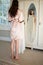 Smiling bride trying on dress while standing by mirror at home