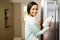 Smiling brunette holding milk bottle with open refrigerator