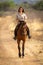 Smiling brunette rides horse along dirt track