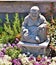 Smiling Buddha statue surrounded by rosemary, greens, and flowers