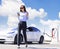 Smiling  business woman walking on city parking near electric car, charging automobile battery from small city station, drinking c