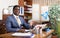 Smiling businessman sitting at desk in office, making inviting gesture