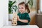 Smiling canny cute child in green dress touching a wooden jenga tower standing on a table