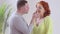 Smiling Caucasian brunette man feeding redhead woman with sweet tasty candy indoors. Side view portrait of loving happy