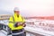 A smiling caucasian builder in a white hard hat and yellow fluorescent jacket holds clipboard