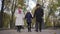 Smiling Caucasian girl walking with her grandparents along the alley in the park. Senior couple dressed in elegant