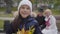 Smiling Caucasian girl in white hat holding a bunch of yellow leaves and looking at the camera. Her grandparent sitting