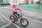 smiling Caucasian preschooler girl riding pink bike bicycle in helmet on backyard road outside on spring autumn day