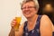 Smiling caucasian senior woman with gray hair holding and drinking glass of light beer in craft czech brewery.