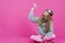 Smiling Caucasian Teenage Girl in Flying Glasses and Knitted Sweater Launching Origami Paper Plane While Posing Over Pink