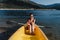 Smiling caucasian woman in swim wear holding oar sitting on yellow canoe in lake during sunny day. summer time. Sports, adventure