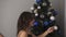 Smiling caucasian young couple decorating the fir tree at home with fancy blue and silver coloured balls. Together fill