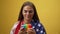 Smiling charming woman playing fidget toy in slow motion standing at yellow background with American flag on shoulders