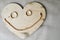 A smiling, cheerful mug made from a wooden heart to Valentine`s Day, wedding gold rings and a female gold chain