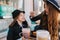 Smiling cheerful woman with light-brown curly hair feeding daughter in black outfit with dainty cake. Portrait of joyful