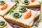 Smiling cheese sandwich with face from cucumbers, tomato, olives and dill