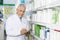 Smiling Chemist Writing On Clipboard While Standing By Shelves