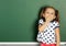 Smiling child girl near empty school blackboard, copy space