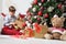 Smiling child unwraps the Christmas gift box near the tree decorated with balls, in living room sitting on the floor near the