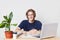 Smiling clever male student wears spectacles and t shirt sits at work place, works on his diploma or course paper, uses modern lap