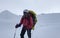 Smiling climber in a helmet, sunglasses, a backpack and trekking poles walks along a snow-covered trail