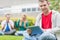 Smiling college boy holding tablet PC with students in park