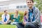 Smiling college boy using tablet PC with students in park